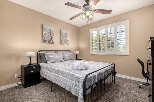 Master bedroom with black bed, patterned bedding, nightstands with lamps, mirrored closet doors, and hardwood floors