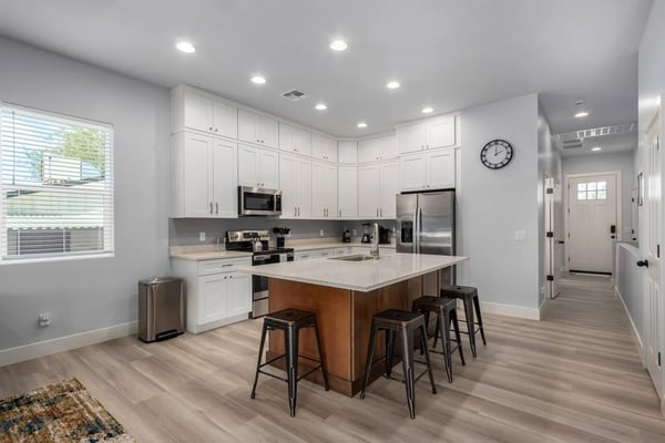 Open-plan kitchen and dining area with white cabinetry, stainless steel appliances, black dining table with orange chairs, and teal accent wall.